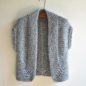 May include: A grey and white knitted cardigan with a wide collar and short sleeves.