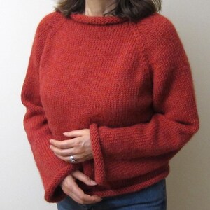 Puede incluir: Un su&eacute;ter de punto color &oacute;xido con cuello redondo y mangas largas. Las mangas tienen un dise&ntilde;o acampanado en los pu&ntilde;os. El su&eacute;ter est&aacute; hecho de un hilo grueso y texturizado y parece hecho a mano. El modelo lleva vaqueros azules.