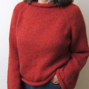 Puede incluir: Un su&eacute;ter rojo tejido con mangas largas y cuello redondo. El su&eacute;ter tiene un ajuste relajado y est&aacute; hecho de un hilo texturizado. La persona lleva vaqueros azules. El su&eacute;ter es de color liso y parece hecho a mano.