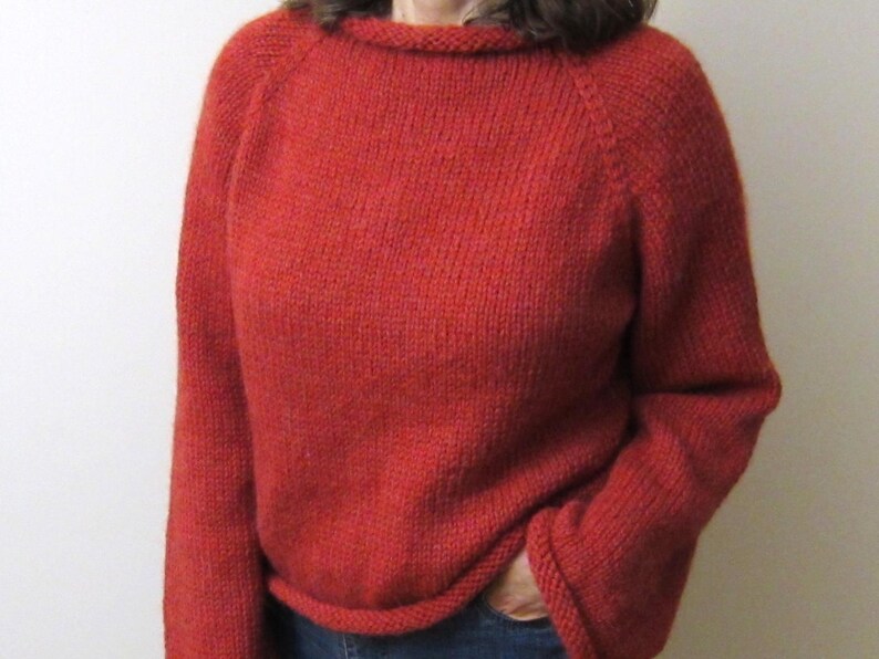 Puede incluir: Un su&eacute;ter rojo tejido con mangas largas y cuello redondo. El su&eacute;ter tiene un ajuste relajado y est&aacute; hecho de un hilo texturizado. La persona lleva vaqueros azules. El su&eacute;ter es de color liso y parece hecho a mano.