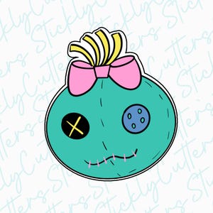 May include: A teal blue plush toy with a pink bow, yellow hair, a black X for an eye, and a blue button with white stitching.