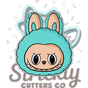 May include: A cartoon-style cookie cutter featuring a monster face with large eyes, a small nose, and a toothy grin. The monster wears a teal hood with matching ears. The text "Street Cutters Co." is visible at the bottom.