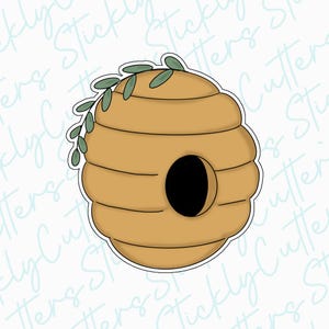 May include: A yellow and brown beehive cookie cutter with a small hole in the front and a green leaf garland on top.