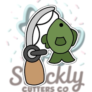 May include: A cookie cutter in the shape of a fishing rod with a green fish attached. The fishing rod is silver and brown, with a black handle. The fish is green with a black eye and a white outline.