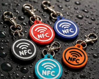 May include: Five circular NFC keychains with metal lobster clasps. The keychains come in black, red, blue, light blue, and orange. Each features a raised white or black wireless signal icon and the text NFC embossed on the front surface.