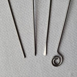 May include: Four silver metal tools with different ends. The tools are arranged in a fan shape on a gray surface.