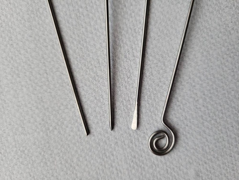 May include: Four silver metal tools with different ends. The tools are arranged in a fan shape on a gray surface.