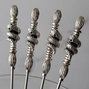 May include: Set of four silver cocktail picks with a snake design and green gemstone eyes.