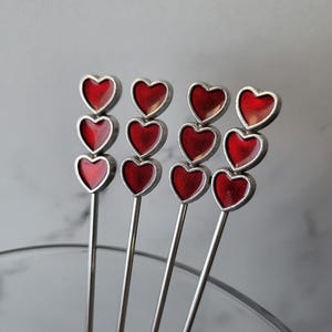 May include: Set of five silver cocktail sticks with red heart-shaped tops.