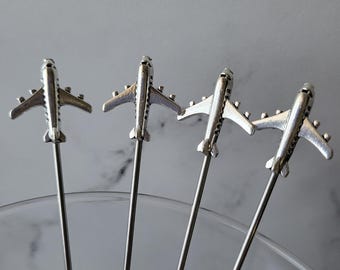 May include: Four silver airplane cocktail picks. The airplane design is on top of a long, thin, silver metal stick.