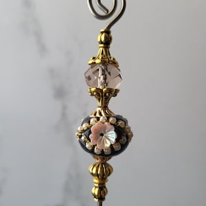 Peut inclure: Une épingle à chapeau décorative avec une base en métal doré et une perle bleu foncé ornée d'une fleur rose et de petites perles blanches. L'épingle présente un cristal clair à facettes et une spirale décorative au sommet.