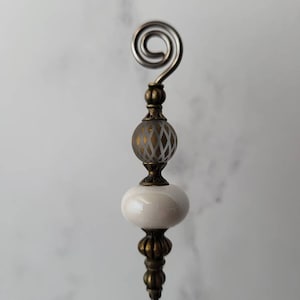 May include: A decorative pin with a white and gold glass bead, a white ceramic bead, and a gold metal swirl at the top.