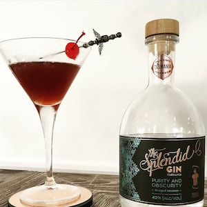 May include: A clear glass bottle of The Splendid Gin from Tasmania. The bottle has a black label with gold lettering and a teal geometric pattern. The label reads "The Splendid Gin, Tasmania, Purity and Obscurity - in equal measure - 42% [ALC/VOL] 700ml".