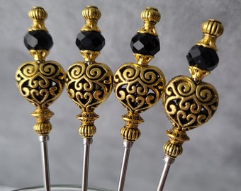 Puede incluir: Juego de cuatro pinchos de cóctel dorados con cuentas de vidrio negras y tapas en forma de corazón adornadas.