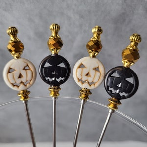 May include: Four gold-tipped, stainless steel cocktail picks with black and white pumpkin-shaped heads. The pumpkins have carved jack-o'-lantern faces.