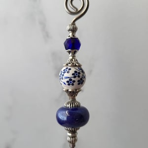 May include: A silver and blue glass bottle stopper with a floral design. The stopper has a loop at the top for easy removal.