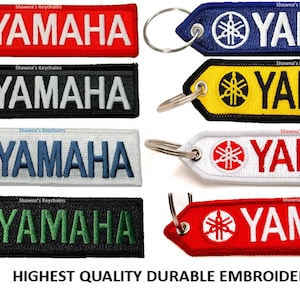 May include: Six different color variations of a Yamaha keychain. Each keychain features a black and white Yamaha logo with a silver key ring. The keychains are red, black, white, blue, yellow, and green.