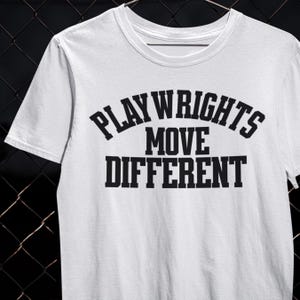 May include: White t-shirt with the text "PLAYWRIGHTS MOVE DIFFERENT" in black, bold, uppercase letters. The shirt has a crew neck and short sleeves. The text is arranged in three lines, with "PLAYWRIGHTS" arched above "MOVE DIFFERENT".