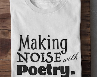Puede incluir: Camiseta blanca con la frase negra "Making Noise with Poetry". La camiseta está doblada sobre una superficie de madera. El texto está escrito en una fuente estilizada.