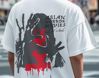 May include: White t-shirt featuring a graphic design with the text "ASIAN HORROR MOVIES Let's talk". The design includes a red face and black hands with dripping effects. The shirt has short sleeves.