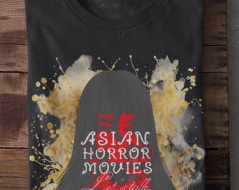 Może przedstawiać: Czarna koszulka z grafiką. Projekt zawiera tekst "ASIAN HORROR MOVIES Let's talk." w kolorze białym i czerwonym, z sylwetką i złotymi rozpryskami.