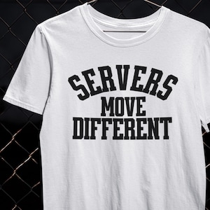 Puede incluir: Camiseta blanca con el texto "SERVERS MOVE DIFFERENT" en negrita, en negro. La camiseta tiene cuello redondo y mangas cortas. El texto está dispuesto en tres líneas, con "SERVERS" en la parte superior.
