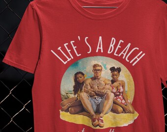 May include: Red t-shirt featuring the text "LIFE'S A BEACH" in white, above a beach scene graphic with three people. The words "stay salty" are printed below. The shirt is made of a soft material.