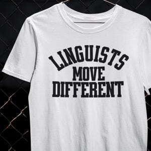 May include: White t-shirt with the text "LINGUISTS MOVE DIFFERENT" in black, bold, uppercase letters. The shirt has a crew neck and short sleeves. The text is arranged in three lines, with "LINGUISTS" arched above "MOVE DIFFERENT".