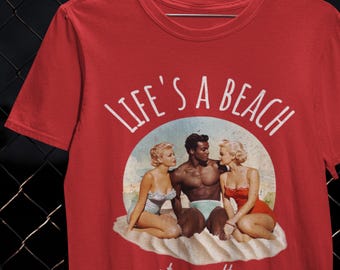 May include: Red t-shirt with the text "LIFE'S A BEACH" and "stay salty". The graphic shows three people in vintage swimwear on a beach scene. The shirt is made of a soft material.