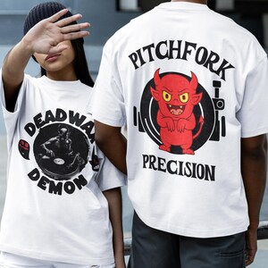 May include: White t-shirts with graphic designs. One shirt features a black and white image of a figure with the text "DEADWA DEMON". The other shirt has a red devil graphic with the text "PITCHFORK PRECISION".