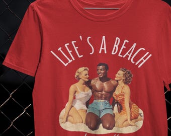 May include: Red t-shirt with the words "LIFE'S A BEACH" in white script. The graphic shows a vintage-style illustration of a muscular man in blue shorts with two women in swimsuits. The words "stay salty" are written below the illustration.