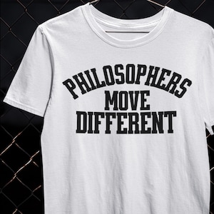 May include: White t-shirt featuring the black text "PHILOSOPHERS MOVE DIFFERENT". The text is in a bold, block font. The shirt has a crew neck and short sleeves. The text is arranged in three lines.