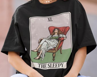 May include: Black XL t-shirt with a tarot card illustration. The card shows a woman in a white dress resting in a red armchair, with the words "THE SLEEPY" below. The design has a vintage style.