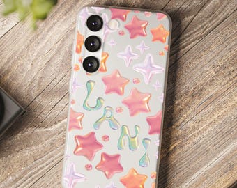 Könnte beinhalten: Transparente Handyhülle mit einem Muster aus rosa, orangefarbenen und lila Sternen. Das Wort "Lani" ist in schillernden Buchstaben geschrieben. Die Hülle liegt auf einer Holzoberfläche, mit einer Kamera und Grünzeug im Hintergrund.