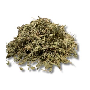 May include: A pile of dried green leaves, possibly herbs or spices, against a white background. The leaves have a textured appearance, with visible stems and varying shades of green and brown. The image is well-lit, highlighting the details of the dried plant material.