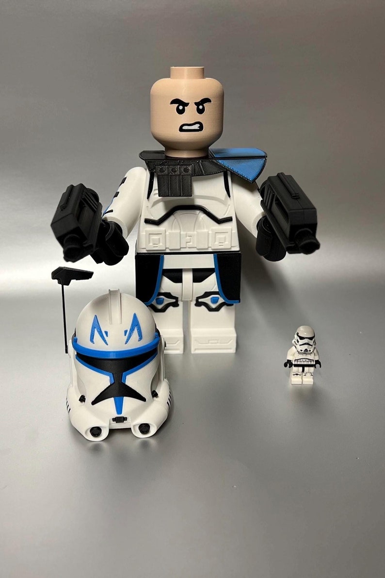 May include: A large white and blue clone trooper action figure with two black blasters, a helmet, and a smaller stormtrooper figure. The clone trooper has a bald head and a stern expression.