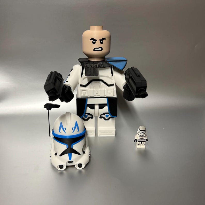 May include: A large white and blue Lego figure with a matching helmet and two black blasters. A smaller Lego figure and helmet are also present. The large figure has a neutral skin tone and is wearing a white and black uniform.