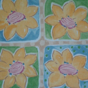 May include: A repeating pattern of watercolor flowers in yellow, pink, and blue. Each flower is set within a square of blue or green, with a tan background featuring small white dots. The floral design has a whimsical, hand-painted aesthetic.