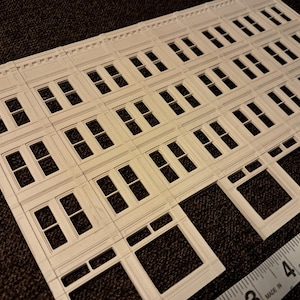 May include: A laser-cut architectural model kit showing building facades with window and door frames. The kit is made of light-colored material and is shown with a ruler, with measurements up to 15 cm.