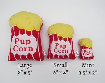 May include: Three plush dog toys shaped like popcorn containers in different sizes. The largest is red with white stripes and says "Pup Corn" in white. It measures 8 inches by 5 inches. The middle toy is red with white stripes and says "Pup Corn" in white. It measures 6 inches by 4 inches. The smallest toy is red with white stripes and says "Pup Corn" in white. It measures 3.5 inches by 2 inches.