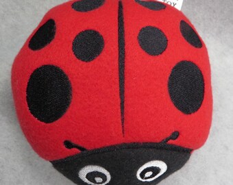 May include: Red ladybug dog toy with black spots and embroidered eyes. The toy has the words "DOG TOY" on a white tag.