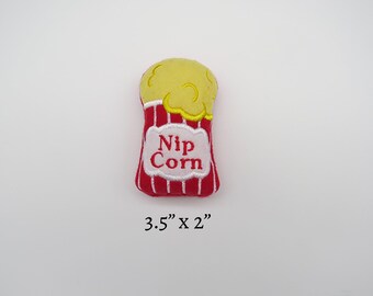 May include: Red and white plush popcorn bag with yellow popcorn on top. The bag says "Nip Corn" and measures 3.5 inches by 2 inches.