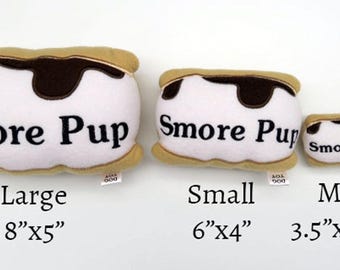 May include: Three plush s'more-shaped dog toys in different sizes: large (8 inches by 5 inches), small (6 inches by 4 inches), and mini (3.5 inches by 2.25 inches). Each toy features a brown chocolate topping, a white marshmallow filling, and a tan graham cracker base. The toys are labeled "Smore Pup".