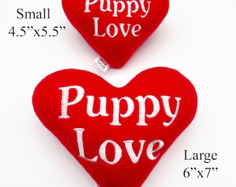 May include: Two red heart-shaped plush dog toys with white embroidery that reads "Puppy Love". The smaller toy is 4.5 inches by 5.5 inches. The larger toy is 6 inches by 7 inches.