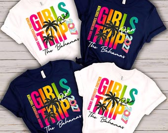 May include: Two white and two navy blue short-sleeve t-shirts featuring a colorful graphic print. The design includes the text GIRLS TRIP, MAKING MEMORIES TOGETHER, The Bahamas, and 2021, along with palm tree silhouettes and the name Rian.
