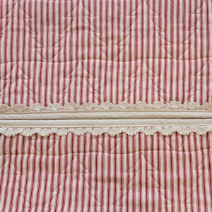 May include: Two red and white striped fabric panels with a white lace trim. The panels are quilted with a pattern of small triangles.