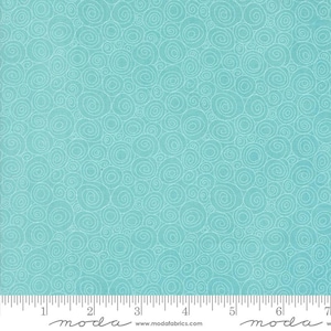 May include: A light blue fabric with a repeating pattern of white swirls. The fabric is marked with a ruler along the bottom edge, with the word "moda" printed at the bottom.
