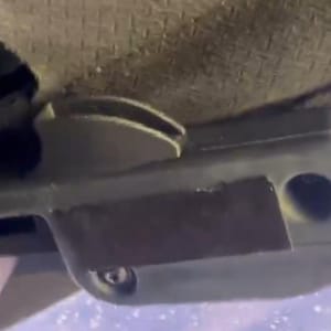 K&ouml;nnte beinhalten: Ein graues mechanisches Bauteil aus Kunststoff mit einem gebogenen Hebel, einem rechteckigen K&ouml;rper mit vertieftem Mittelteil und einer kreisf&ouml;rmigen &Ouml;ffnung auf der rechten Seite. Eine kleine Metallschraube ist am unteren Rand sichtbar.