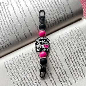 May include: A black and pink beaded keychain with a charm that says "Drink Coffee Read Smut Be Happy". The charm features a skull and crossbones with a coffee cup and a book.