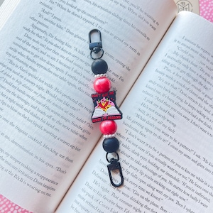 May include: A red and black beaded keychain with a charm that says "Don't F*ck With Me What I'm Reading". The charm is a cartoon image of a pig wearing a crown and reading a book.